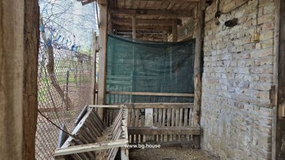 Covered farm enclosure featuring wooden feeding trough and wire mesh fencing for livestock.