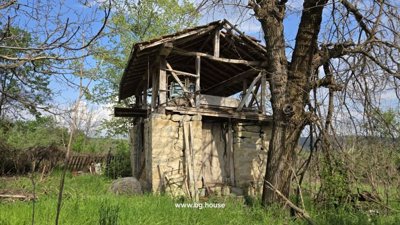 Traditional outbuilding made of stone and wood with an upper wooden structure and tiled roof in the garden.