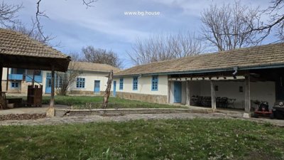 Exterior view of a traditional Bulgarian house with blue doors and windows and a tiled roof surrounded by leafless trees.