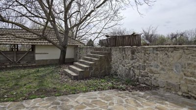 Stone staircase ascending to a raised stone terrace enclosed by a wooden fence, with leafless trees surrounding the area.