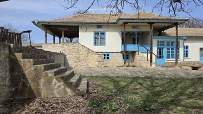 Stone stairs leading up to a covered balcony with blue wooden railings and windows on a traditional house.