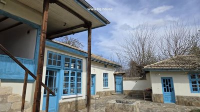Stone paved courtyard featuring blue doors and windows with a wooden door opening to a garden area.