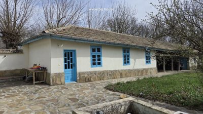 Traditional house walls with blue doors and windows next to a covered sitting area with wooden posts.