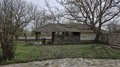 Wooden gazebo with a tiled roof located in the garden surrounded by trees and greenery.
