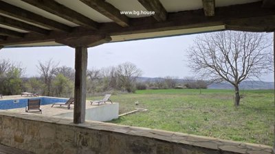 View from the veranda showing a swimming pool with sun loungers and an open grassy field beyond.