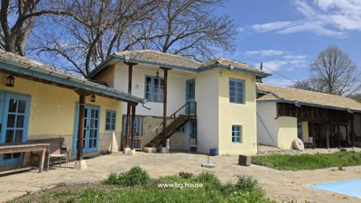 Traditional Bulgarian rural house with stone roof and blue window frames surrounded by trees