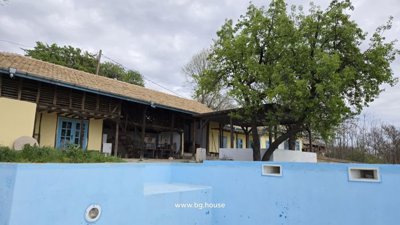 View of the rustic house exterior featuring yellow walls, blue doors, and an empty blue swimming pool in the foreground.