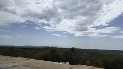 Expansive view of rolling hills and scattered trees beneath a partly cloudy sky in rural Bulgaria.