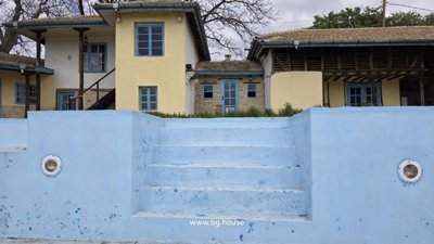 Front facade of the rustic house with yellow walls and blue doors, viewed from the empty blue swimming pool with steps.