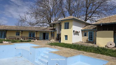 Yellow rural house with blue doors and windows beside an empty blue swimming pool