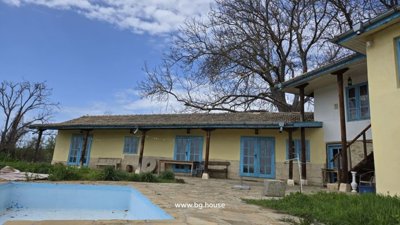 Yellow rural house with blue windows and empty swimming pool with stone patio and grass
