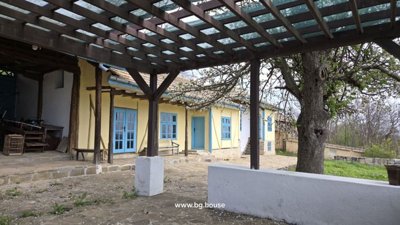 Yellow rural house with blue windows and empty swimming pool with stone patio and surrounding trees