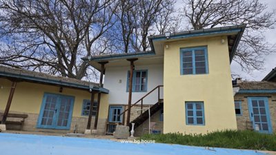Covered outdoor terrace with wooden pergola next to yellow house with blue windows