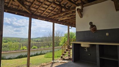 Covered veranda showing wooden beams and open view of green countryside beyond a low wall.