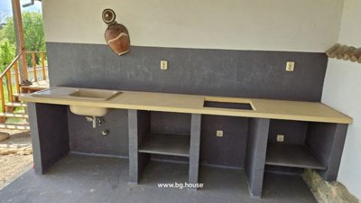 Outdoor kitchen area featuring a long counter with a sink and multiple open storage compartments below.