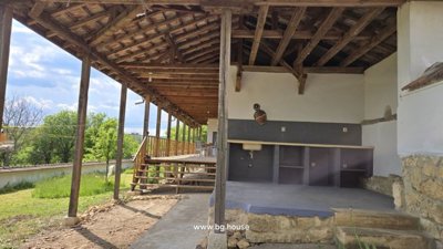 Covered outdoor kitchen space featuring stone base counters and a wooden roof structure