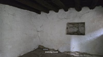 An empty room featuring whitewashed walls with cracks and exposed dark wooden ceiling beams.
