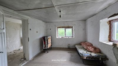 A room with two windows, a foldable bed frame with mattress and bedding, and wooden floorboards.