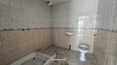 Bathroom interior showing tiled walls and floor, a toilet bowl, a wall-mounted basin, and a shower tray without fittings.