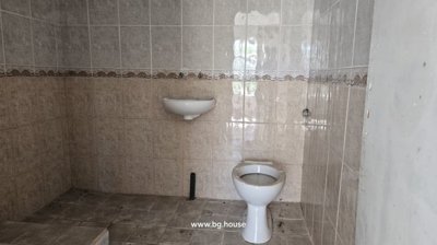 View of a bathroom with beige and cream tiles on walls and floor, a toilet bowl, and a wall-mounted basin.