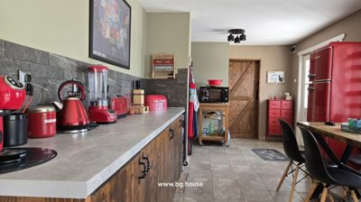 Kitchen interior featuring red appliances including a kettle, toaster, and refrigerator alongside wooden cabinets and tiled floor.