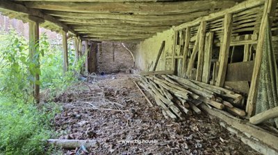 View inside the covered outdoor storage space showing wooden beams, stacked logs, and scattered debris on the ground