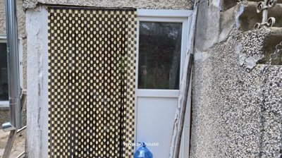 White entrance door partially covered by a decorative hanging curtain beside textured exterior wall
