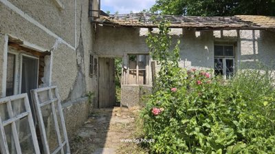 Outdoor passage beside the Bulgarian house showing old windows stacked against the wall and garden plants growing alongside