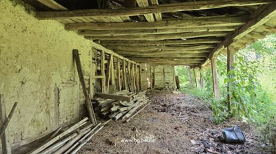 Covered outdoor storage area featuring wooden beams, stacked logs, and a dirt floor, part of the property outbuildings