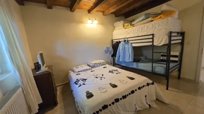 Bedroom showing a double bed, metal bunk bed, stacked mattresses, and a wooden ceiling with exposed beams.