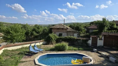Outdoor swimming pool with clear blue water and two blue double sun loungers set on stone paving near garden greenery.