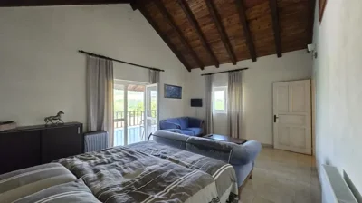 Bright bedroom with double bed, blue sofa, high wooden ceiling, and doors opening to a balcony with views.