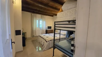 Bedroom with a double bed, metal bunk bed, window with light curtains, and radiator below the window.