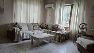 Living room featuring a corner sofa covered with throws and cushions, a rustic coffee table, armchair, and large window with curtains.