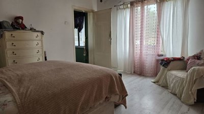 Bedroom featuring a double bed covered with a knitted blanket and a window with sheer curtains providing soft daylight.