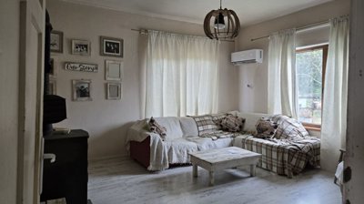 Living room interior with white walls, a corner sofa with plaid covers, a wood stove, and framed photos on the wall.