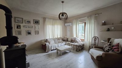 Living room interior with white walls, a corner sofa with plaid covers, a wood stove, and framed photos on the wall.