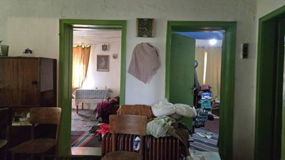 View through green door frames showing two rooms with chairs, a wardrobe, and household items