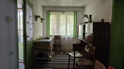 Interior room featuring a table, chairs, glass cabinet, and a large window with green frame and curtains