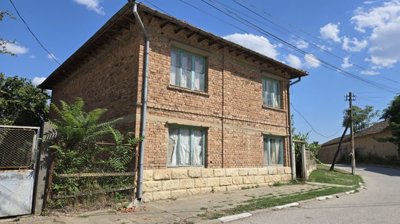 Corner perspective of a brick house showing green window frames and a metal gate entrance