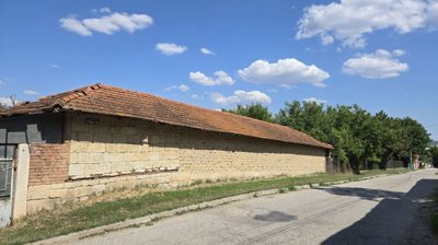 Long brick outbuilding with tiled roof situated along a quiet street with trees behind