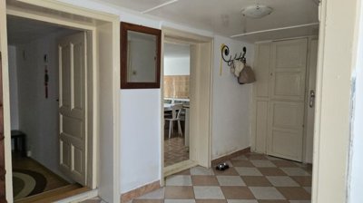 Interior hallway featuring beige and white checkered tiled floor, several doorways, a wall mirror, and a coat rack with hanging items.
