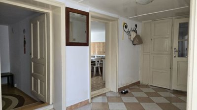 Interior hallway featuring beige and white checkered tiled floor, several doorways, a wall mirror, and a coat rack with hanging items.
