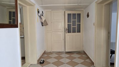 Interior hallway featuring beige and white checkered tiled floor, several doorways, a wall mirror, and a coat rack with hanging items.