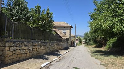 Street view showing a stone wall and metal fence running along the sidewalk beside the house.