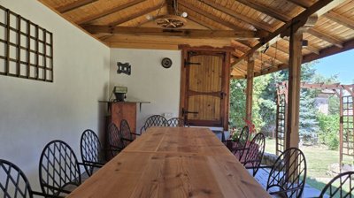 Covered outdoor dining area with a long wooden table, chairs, and wooden ceiling beams.