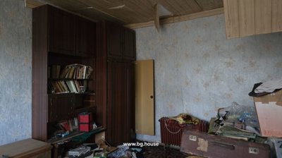 Interior view of a room with wallpapered walls, a wooden wardrobe, and clutter on the floor and furniture.