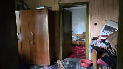 Room featuring a large wooden wardrobe and a cluttered sofa with an open door to another room