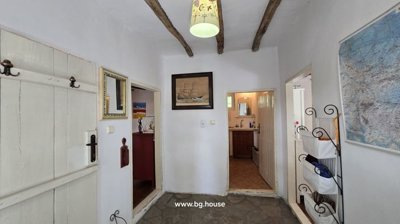 Hallway featuring white walls, exposed wooden ceiling beams, stone flooring, and doorways leading to other rooms