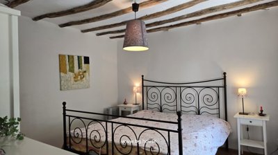 Bedroom furnished with a black metal bed frame, two white bedside tables with lamps, and abstract wall art